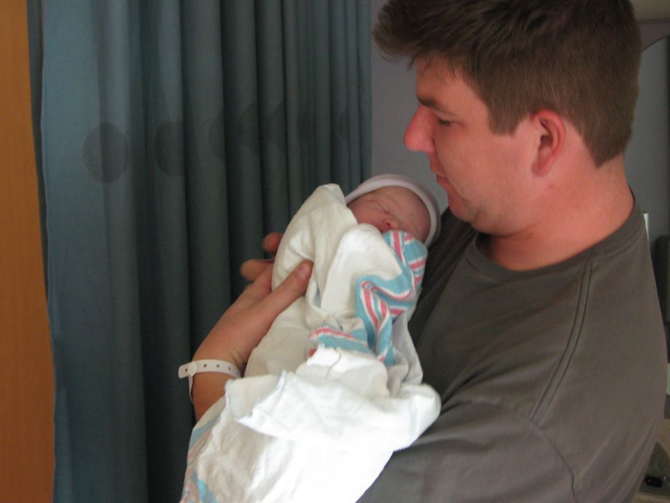 Man holding a swaddled newborn baby. Baby wears a white hat