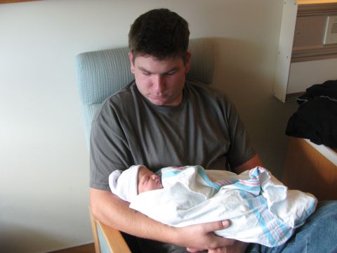 1987 Suzuki Samurai - A man cradles a newborn baby wrapped in a blanket and hat.