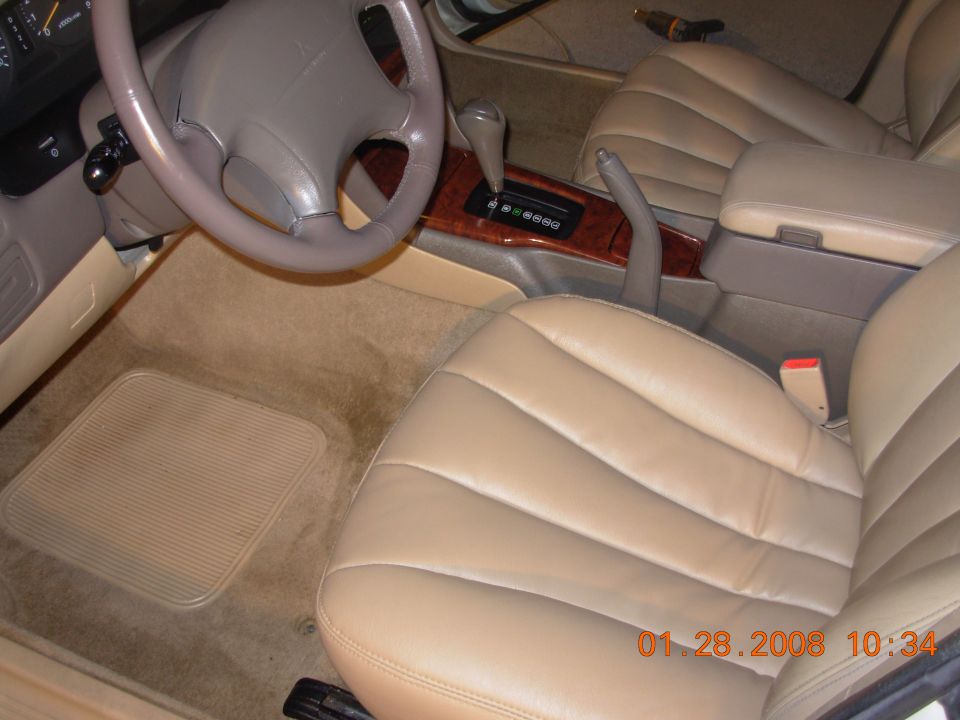 Tan leather car interior with wood trim on the center console and a floor mat
