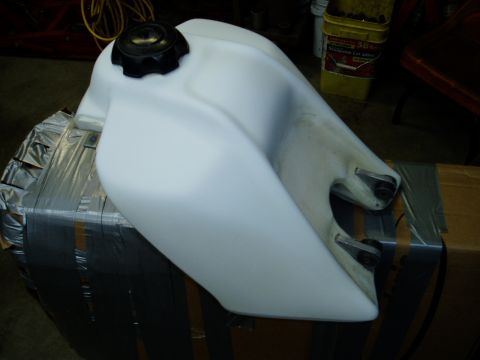 2000 Ford E350 - A white plastic fuel tank with a black cap is shown from a side angle, resting on a box.