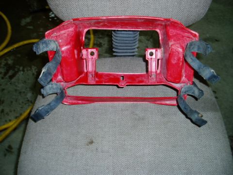 2000 Ford E350 - Red plastic part with black straps, possibly a grille surround or bumper component.