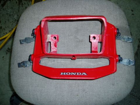 2000 Ford E350 - A red plastic Honda part, possibly a headlight bezel, is shown against a textured background.