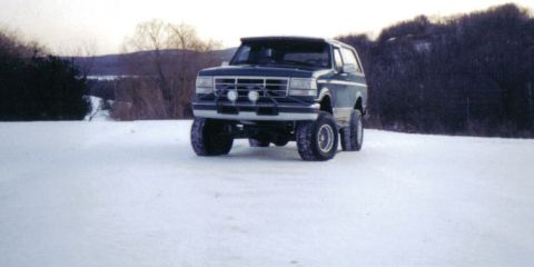 1996 Ford Bronco - A lifted Ford Bronco sits in a snowy field with trees and hills in the background.