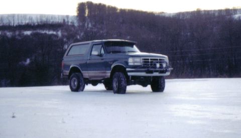 1996 Ford Bronco - A dark blue Ford Bronco sits in a snow-covered field with trees in the background.