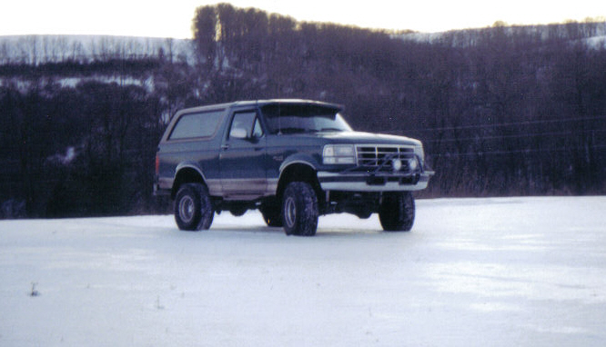 Dark blue Ford Bronco with a light brown stripe, parked in a snowy field