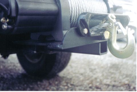 1996 Ford Bronco - Tight low-angle shot of a black electric winch with steel cable wound on the drum, bolted to a fabricated steel mounting plate under a fron…