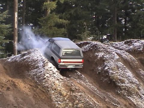1994 Ford Explorer - A Ford Bronco II navigates a steep, snowy dirt incline, kicking up dust and smoke.