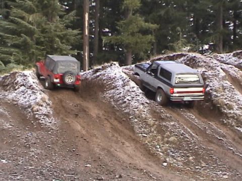 1994 Ford Explorer - A gray 1989 Ford Bronco II navigates a steep dirt incline, with a red Jeep visible behind it.