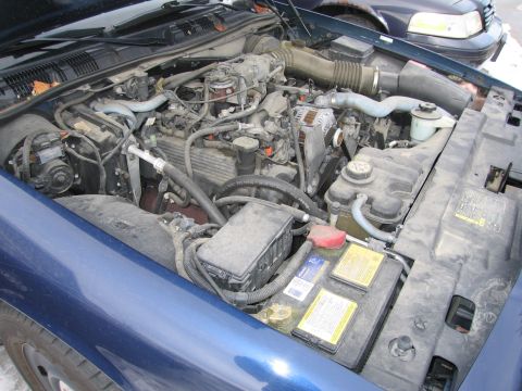 1991 Ford LTD Crown Victoria - The engine bay of a blue Ford Crown Victoria, showing the battery and various engine parts.