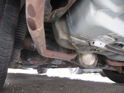 1991 Ford LTD Crown Victoria - A low-angle view of a vehicle's undercarriage, revealing the exhaust system, rear differential, and a portion of the tire.