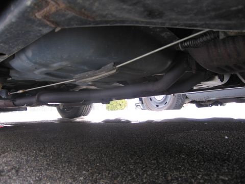 1991 Ford LTD Crown Victoria - Underside view of a car's fuel tank and exhaust system, with a wheel visible.