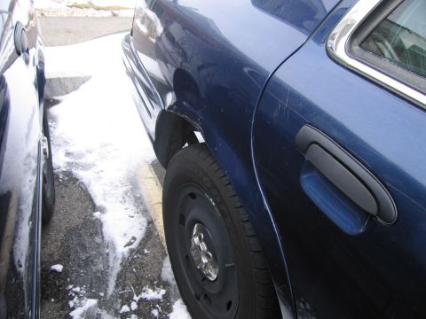 1991 Ford LTD Crown Victoria - Side view of a blue sedan's rear door and wheel, partially covered in snow. The vehicle appears to be a 1991 Ford Crown Victoria LTD.