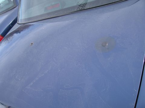 1991 Ford LTD Crown Victoria - The rear of a blue car shows a circular mount and a small hole on its dusty surface.