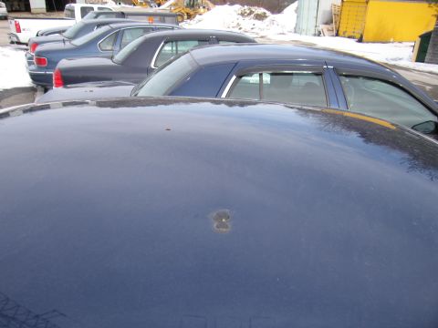 1991 Ford LTD Crown Victoria - A dent is visible on the hood of a dark blue sedan parked in a lot with other vehicles.