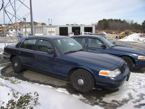 1991 Ford LTD Crown Victoria - Two dark blue sedans are parked in a lot with snow on the ground. One car is in the foreground.