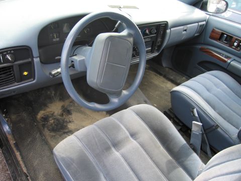1991 Ford LTD Crown Victoria - The interior of a car shows worn blue seats and a dirty floor, with a view of the dashboard and steering wheel.
