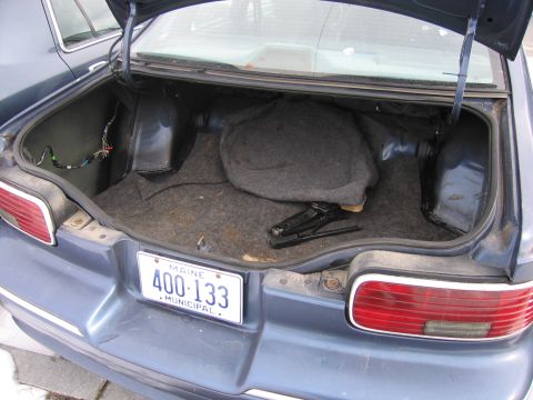 1991 Ford LTD Crown Victoria - The trunk of a blue sedan, showing the spare tire cover, jack, and wiring. A Maine license plate is visible on the rear bumper.
