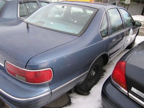 1991 Ford LTD Crown Victoria - A blue sedan is parked next to another vehicle in the snow. The rear of the sedan is visible.