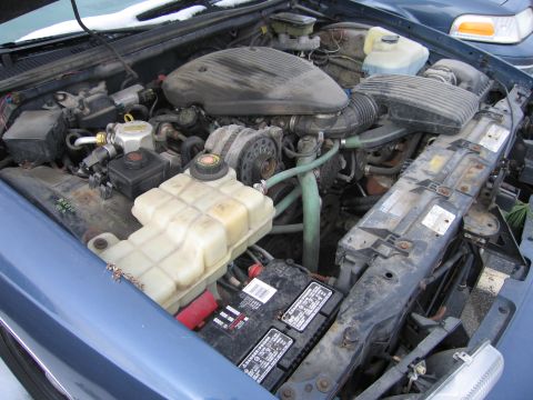 1991 Ford LTD Crown Victoria - The engine bay of a blue car, showing various components and a second vehicle in the background.