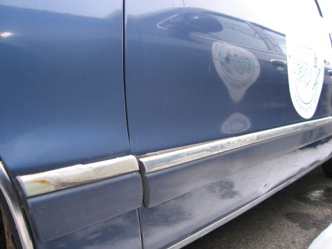 1991 Ford LTD Crown Victoria - Side view of a blue car showing door panel details and a reflected emblem on the paint.
