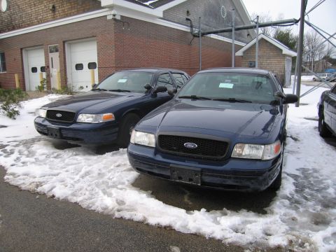 1991 Ford LTD Crown Victoria - Two dark blue Ford Crown Victorias are parked in the snow outside a brick building.