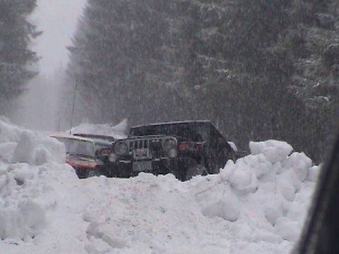 1994 Ford Explorer - Two SUVs are stuck in deep snowdrifts on a road, with trees in the background.