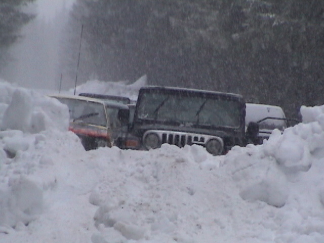 Black Jeep Wrangler parked among deep snowbanks during heavy snowfall