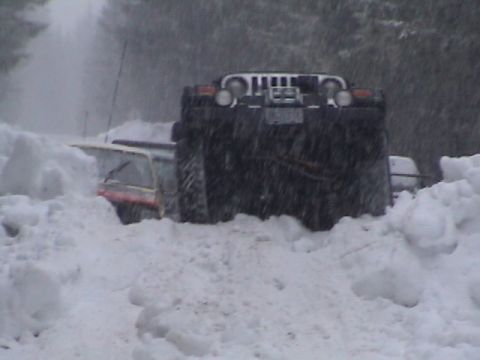 1994 Ford Explorer - A black Jeep Wrangler is stuck in deep snow, with another vehicle partially visible to its left.