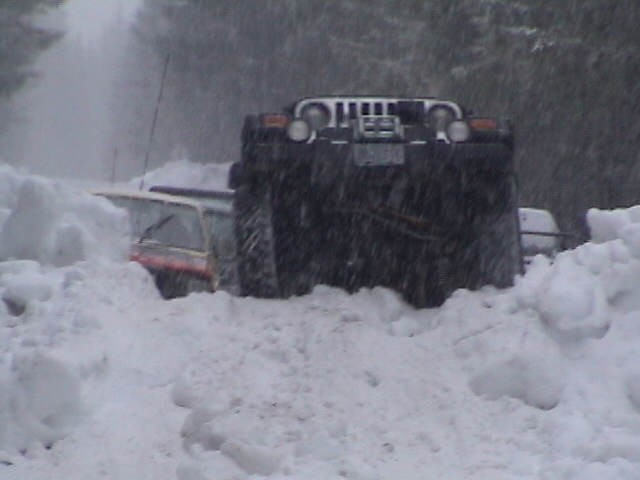 Dark 4x4 with chrome grille climbing a deep snowbank in falling snow