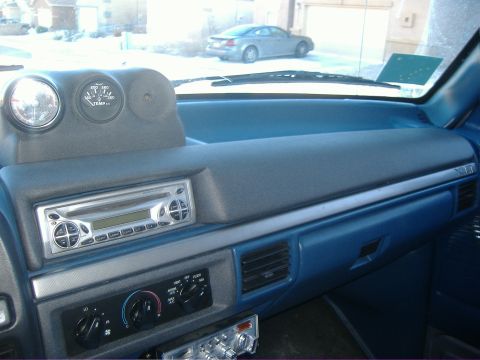 1995 Ford Bronco - The interior of a vehicle shows the dashboard with aftermarket gauges and a stereo system, with a car visible outside.