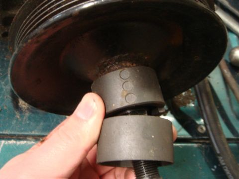 1996 Ford Bronco - A hand is shown using a tool to remove a pulley, which has three circular markings.