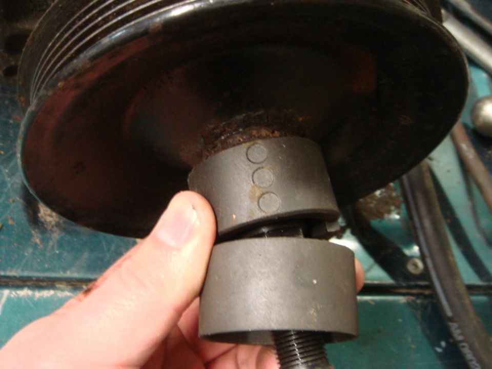 Hand holding a pulley removal tool on a pulley with three circles marked on it
