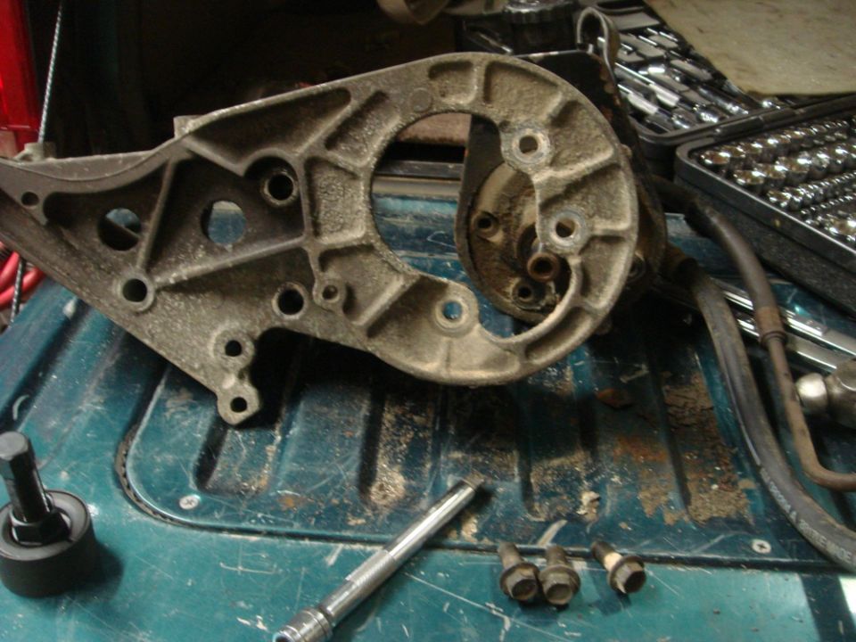 Cast aluminum power steering pump bracket with bolts and a socket extension on a teal surface
