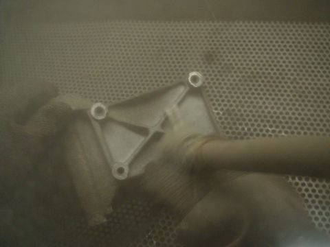 1996 Ford Bronco - A metal bracket with a pipe is being processed in a dusty environment.