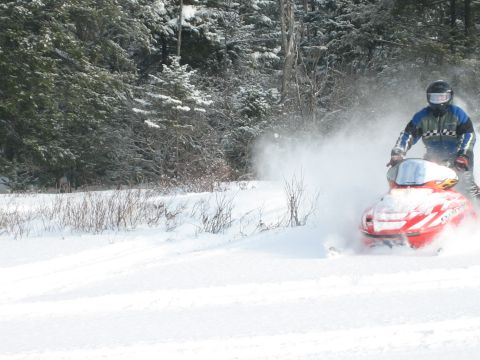 1995 Ford Bronco - Snowmobile rider kicks up a cloud of snow while riding through a wooded area.