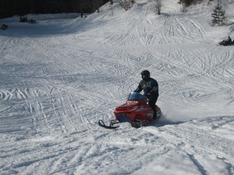 1995 Ford Bronco - A rider navigates a snowmobile down a groomed slope, leaving tracks in the snow.