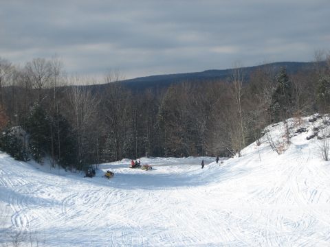 1995 Ford Bronco - Several snowmobiles are parked and in use on a snow-covered hill, with a wooded area and distant hills under a cloudy sky.