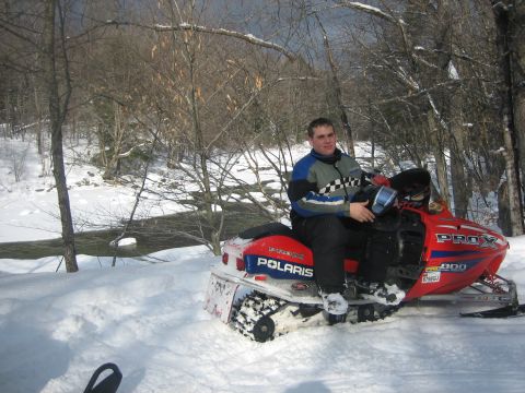 1995 Ford Bronco - A man poses on a red Polaris snowmobile in a winter landscape with trees and a stream.
