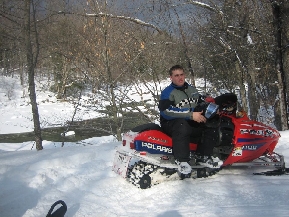 Man sitting on red Polaris snowmobile in snowy woods