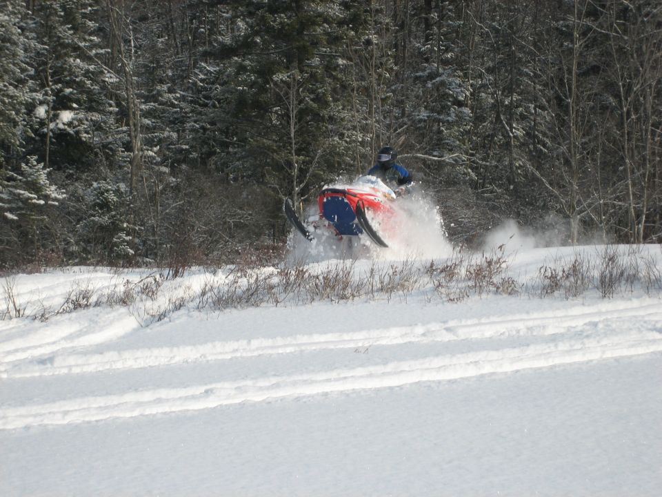 Red and blue snowmobile kicking up snow on a snowy track, side view