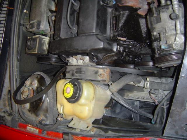 Engine bay with yellow coolant reservoir and black hoses. Belts and pulleys are visible