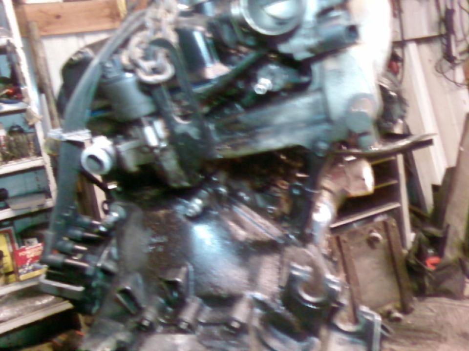 Dark greasy engine block on chain hoist in cluttered garage workshop