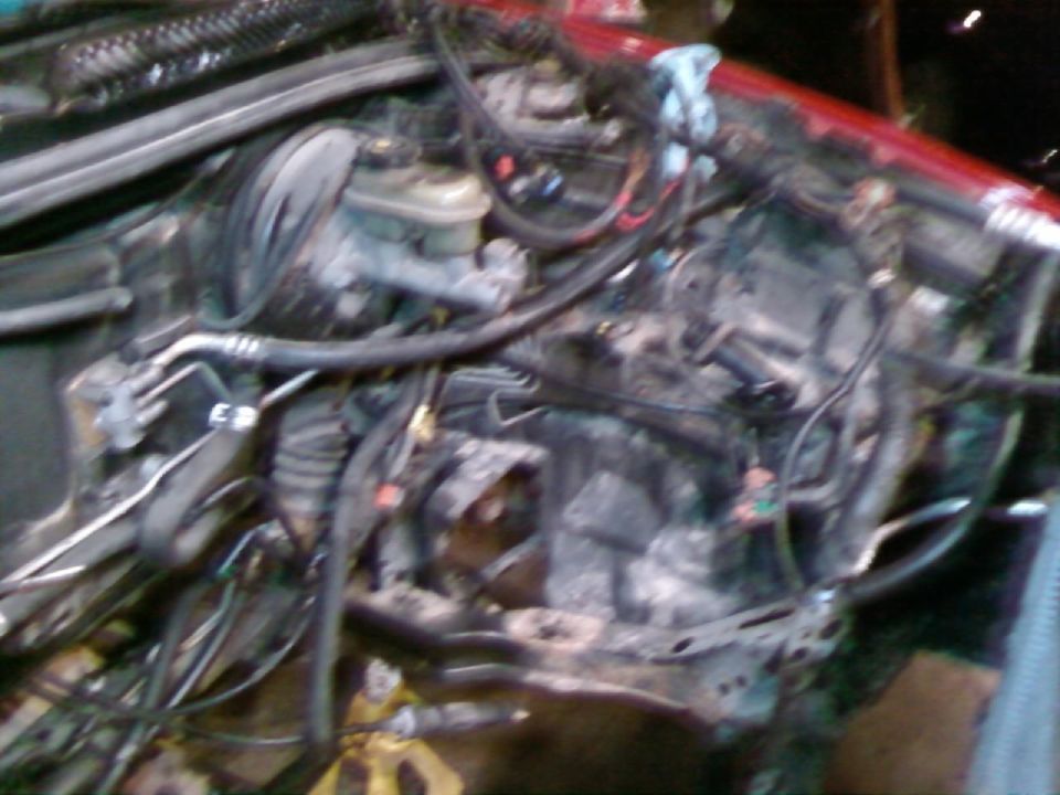 Engine bay of a red car with engine removed, master cylinder and loose wiring visible