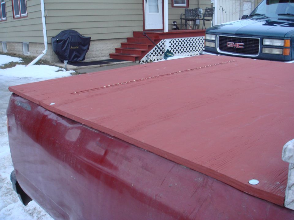 Red wooden truck bed cover over a red truck bed. GMC truck visible in background