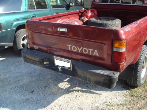 1991 Toyota Tacoma - Rear view of a red 1991 Toyota pickup truck, showing the tailgate with "TOYOTA" lettering and a V6 badge.
