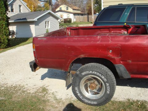 1991 Toyota Tacoma - Rear view of a red 1991 Toyota Tacoma pickup truck with a green SUV behind it.