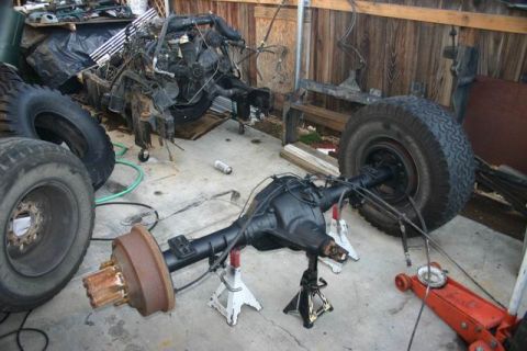 1991 Ford Bronco - Front axle assembly and engine components are disassembled and supported by jack stands in a garage setting.