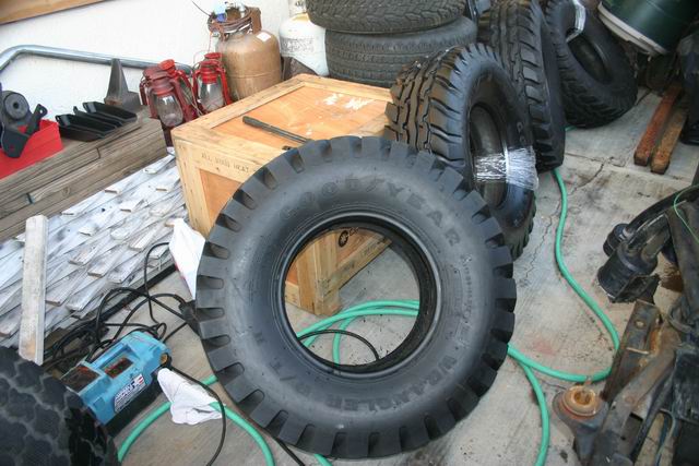 Pile of tires, including a Goodyear Wrangler, with various automotive parts and a wooden crate