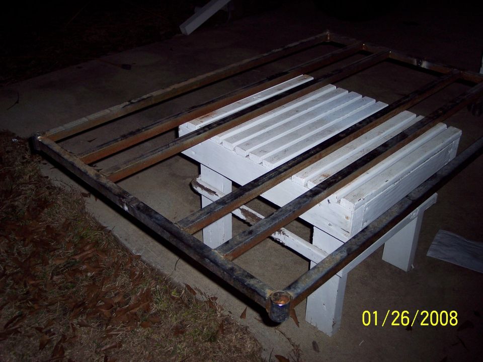 Metal rack frame with wooden slats on white sawhorses, outdoors at night