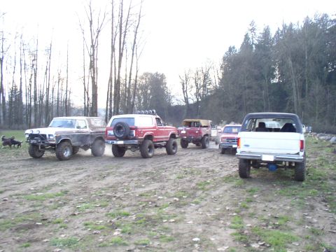 Line of lifted Ford trucks and Broncos parked on a muddy field at a meet